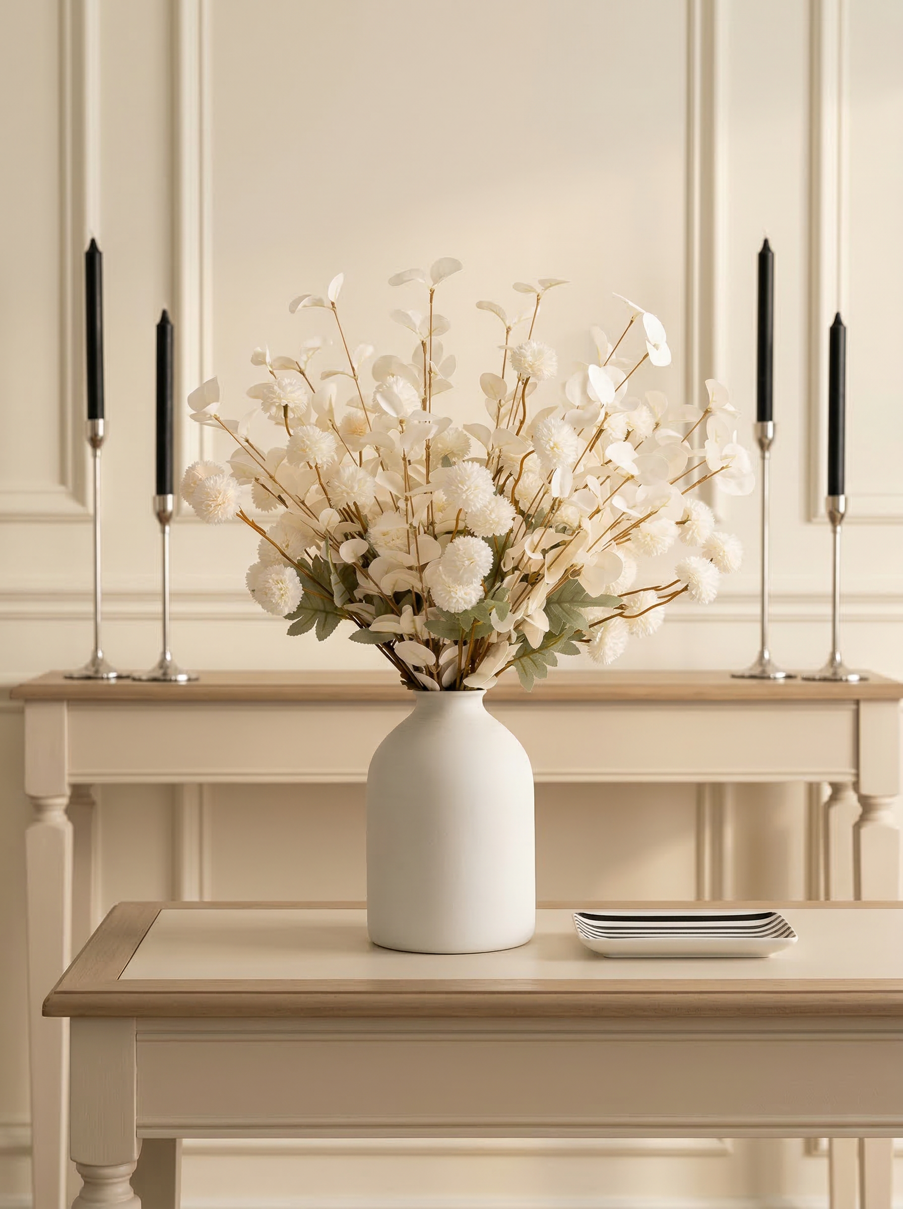 White vase with decorative flowers on a wooden table against a neutral wall.