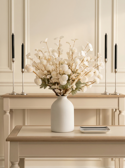 White vase with decorative flowers on a wooden table against a neutral wall.