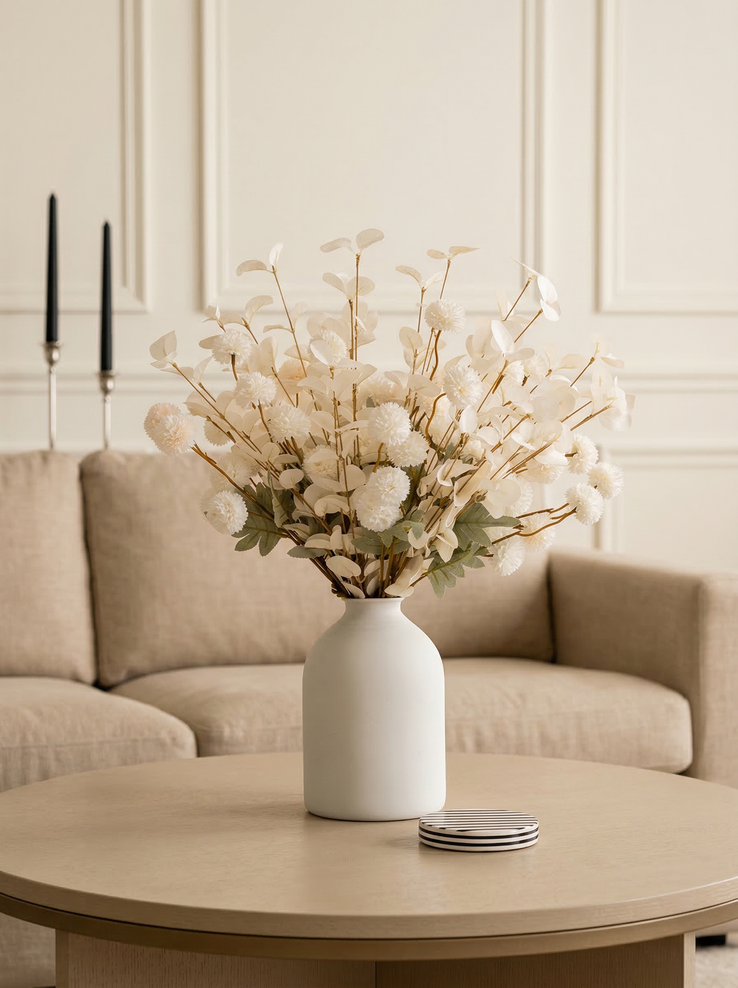 White vase with dried flowers on a wooden coffee table in a living room.
