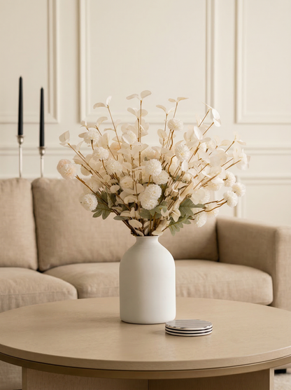 White vase with dried flowers on a wooden coffee table in a living room.
