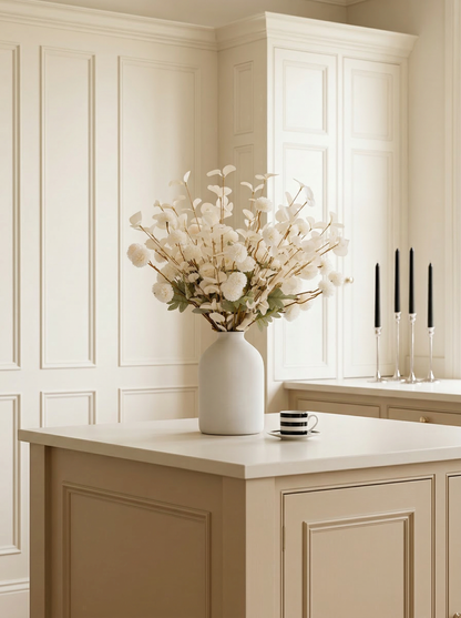 White vase with flowers on a kitchen counter with light-colored cabinets.